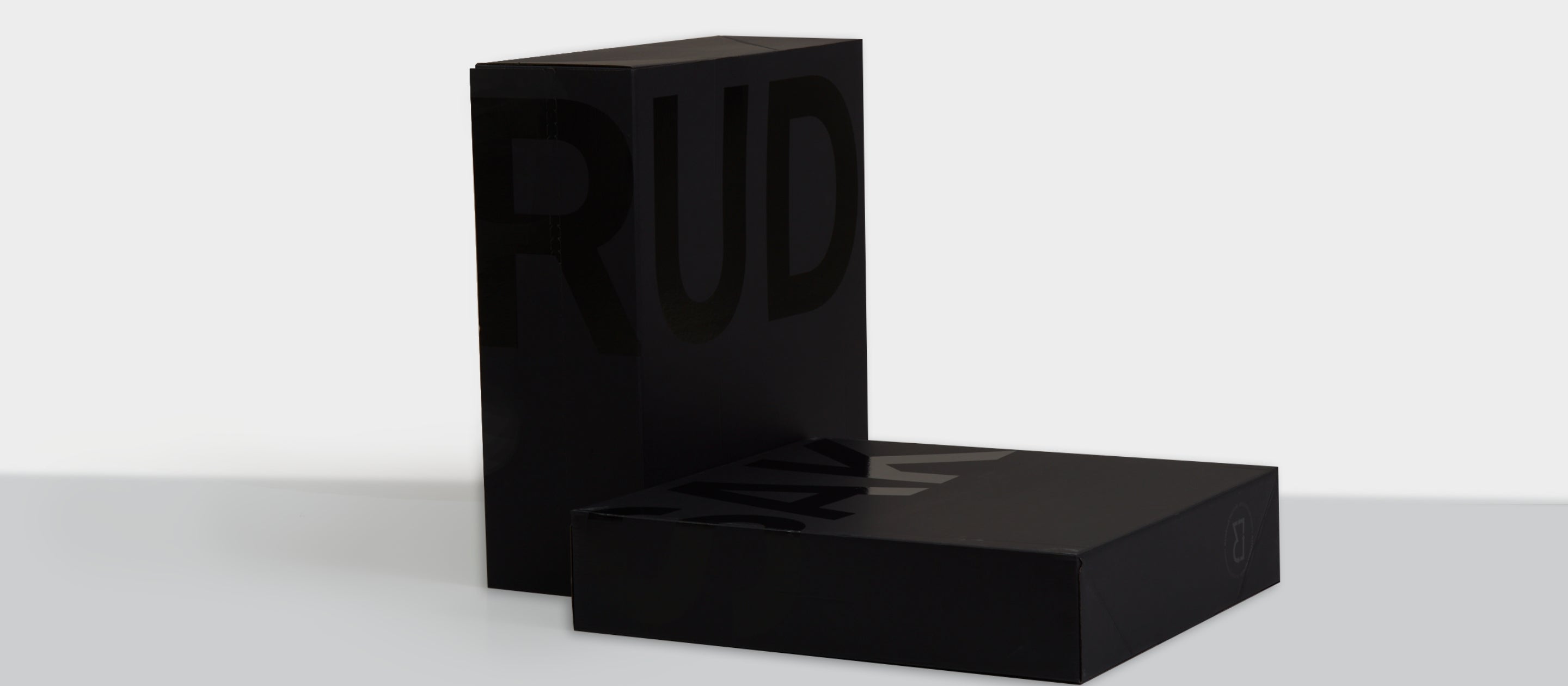 Two sleek black boxes with glossy, partially visible large letters on their surfaces. One box stands upright while the other lies flat, both set against a plain white background.