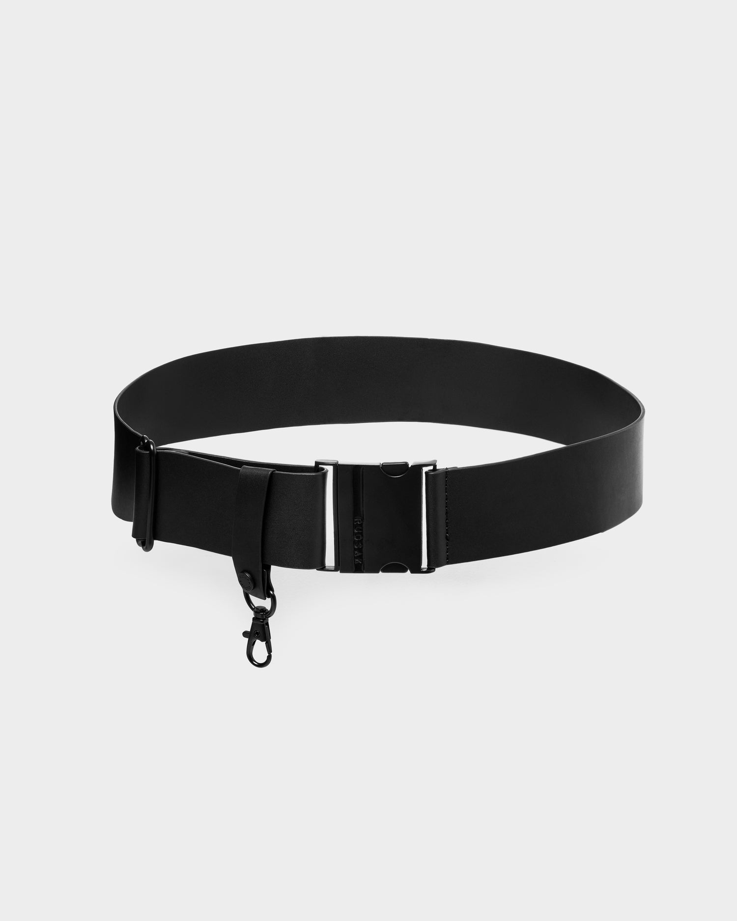 The Rudsak LOTUS - 8425002 Black is a minimalist black belt with a metal buckle and small attached hook, shown on a plain white background.