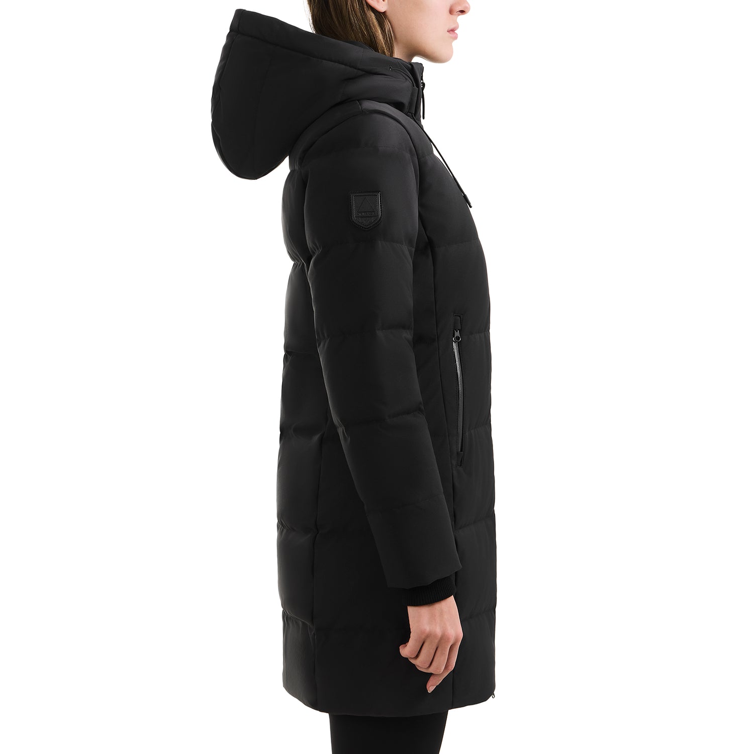 A person models the Rudsak SYDNEY COM - 4123511 Black, a black hooded quilted duck-down parka with a water-repellent finish, zippered side pockets, and an upper arm patch, shown in profile against a white background.