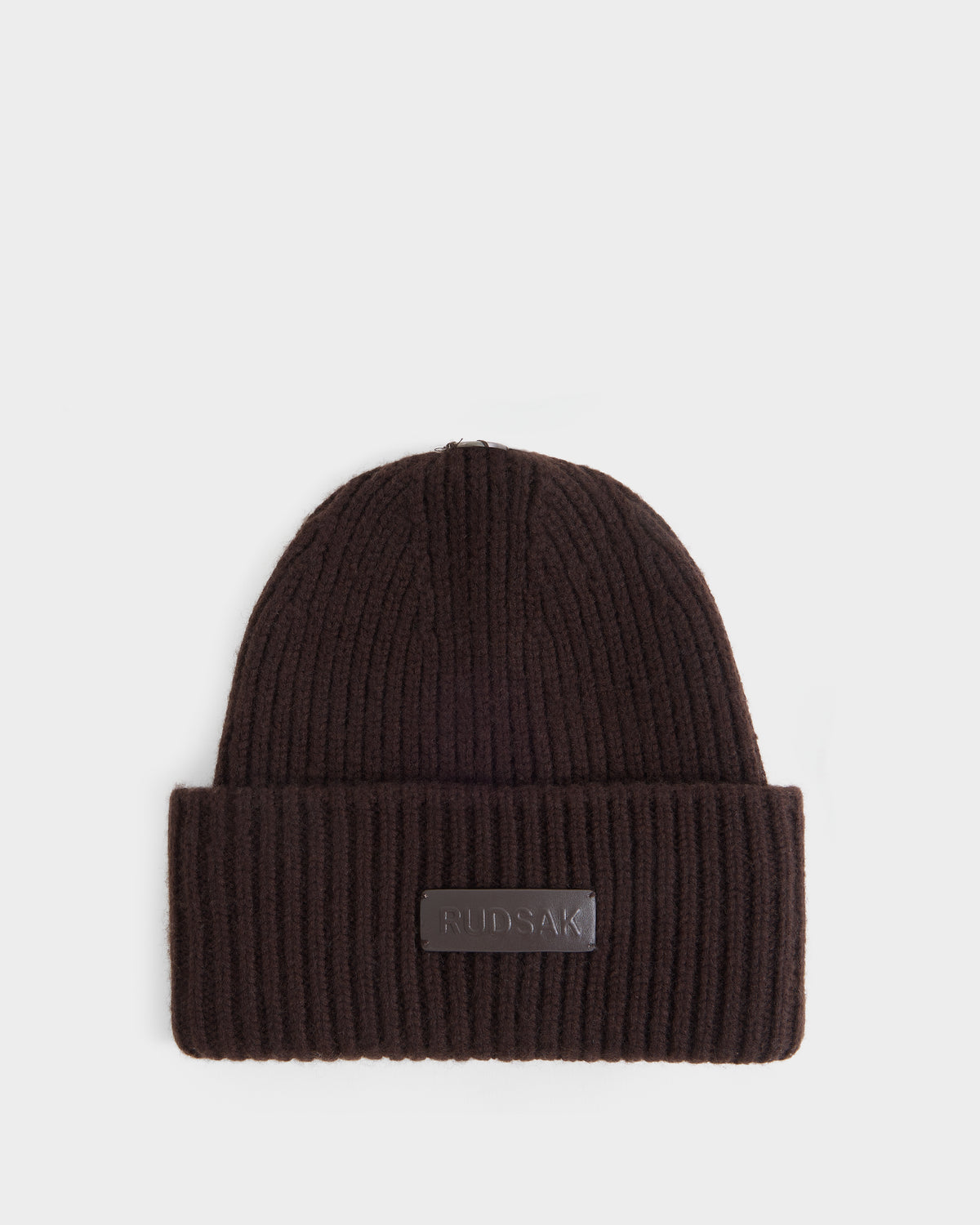A stylish women’s winter hat, the DARA - 8425019 Espresso by Rudsak, features a ribbed knit design in espresso brown with a folded brim and a rectangular Rudsak label on the front, displayed on a plain white background.