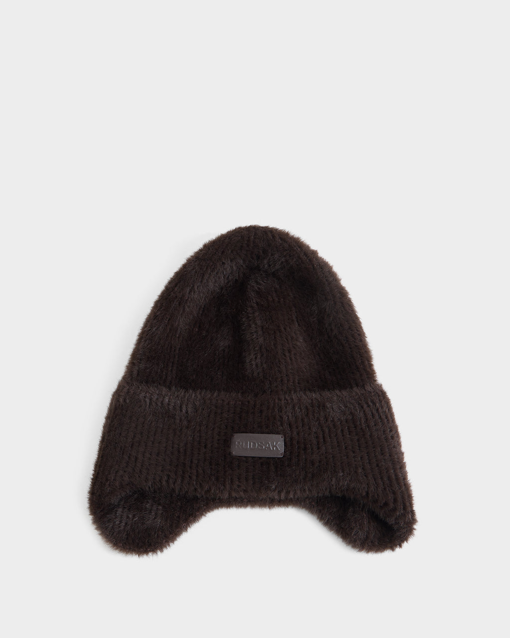 A plush espresso-colored winter hat with ear flaps and a folded brim, featuring a small rectangular patch on the front, from Rudsak’s ICE - 8426519 collection, displayed on a plain white background.