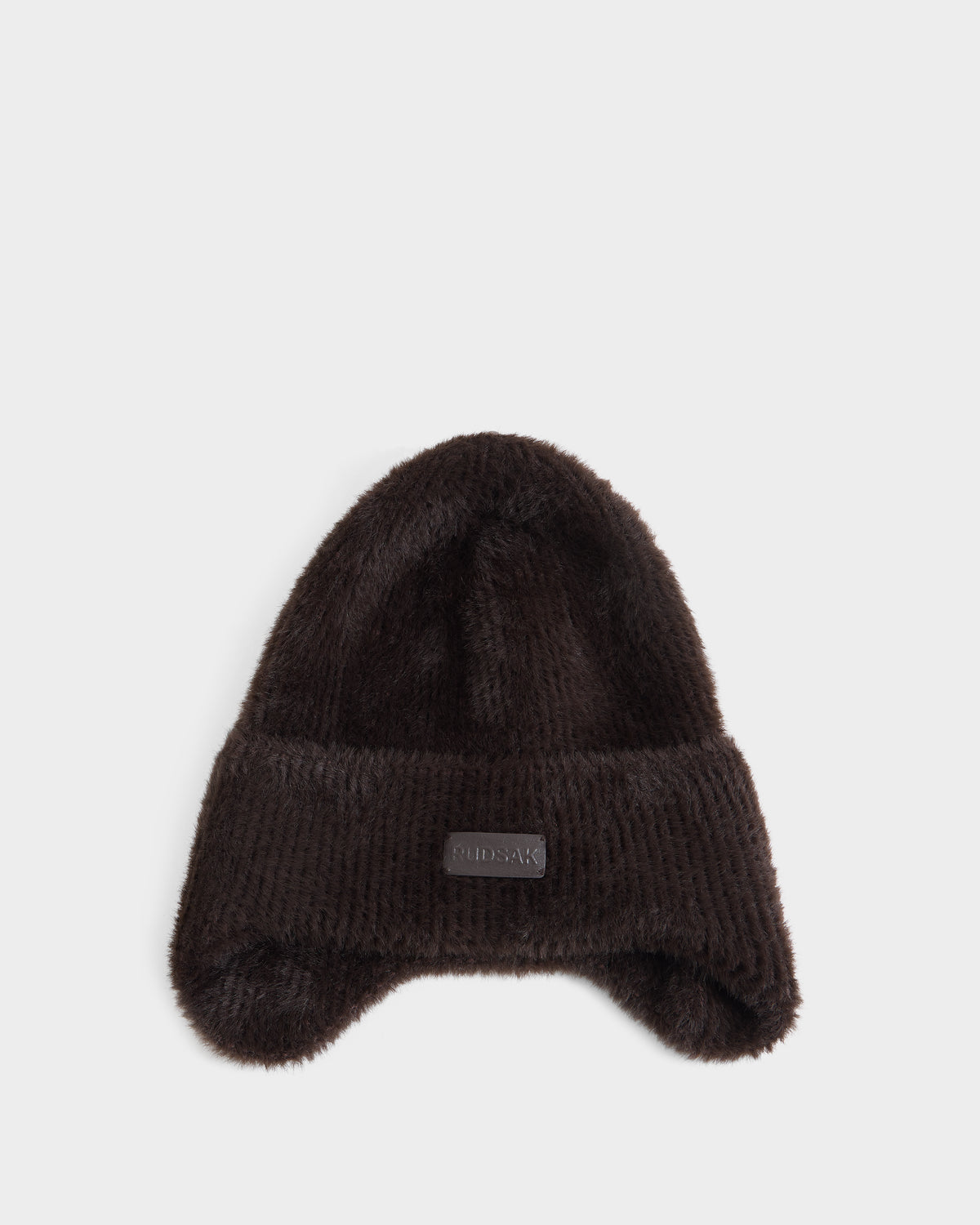 A plush espresso-colored winter hat with ear flaps and a folded brim, featuring a small rectangular patch on the front, from Rudsak’s ICE - 8426519 collection, displayed on a plain white background.