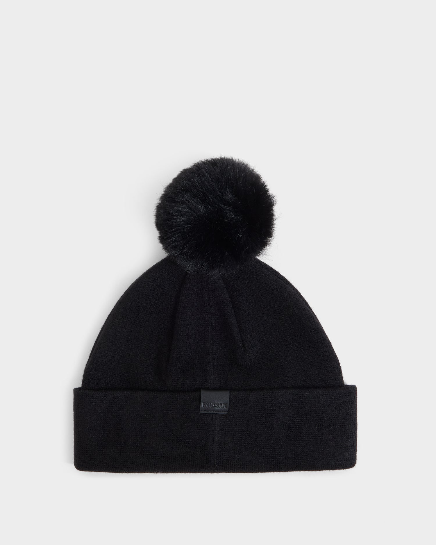 The Rudsak ESTELLA - 8426521 Black beanie features a large faux fur pom-pom on top and a folded cuff, shown against a plain white background.