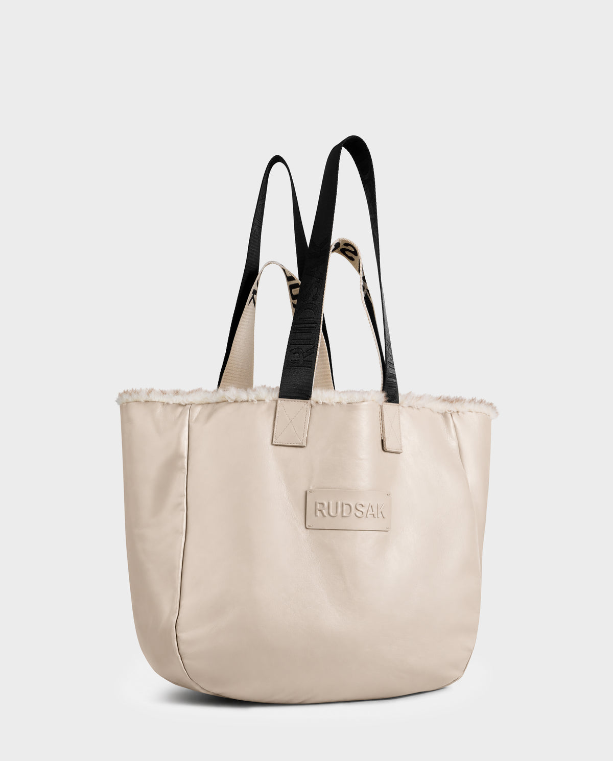 Rudsak ANNIAH - 8325541 Vanilla/Mix Vanilla cream-colored reversible tote bag with a faux-shearling trimmed opening, black fabric handles, and a rectangular patch on the front.