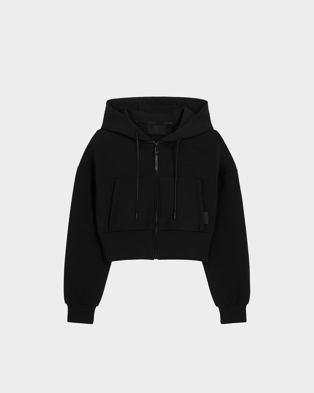 The Rudsak ALAYA - 8525038 Black is a women’s cropped zip-up hoodie with front pockets, drawstrings, and long sleeves for a casual-chic look, shown against a plain light gray background.