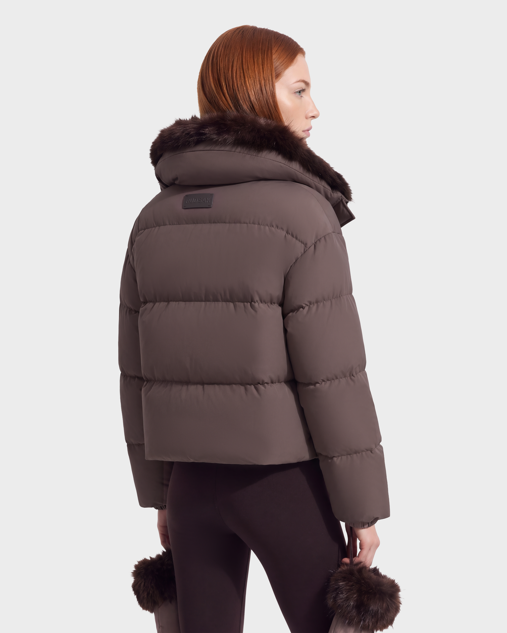 A person seen from behind wearing the ALONDRA - 8126992 Espresso cropped puffer jacket in brown with a dark fur-trimmed collar and matching fur-trimmed cuffs.