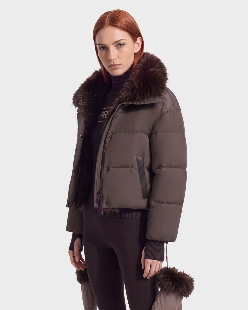 A woman wears a cropped espresso-colored ALONDRA - 8126992 Espresso puffer jacket featuring a dark brown fur collar and cuffs.