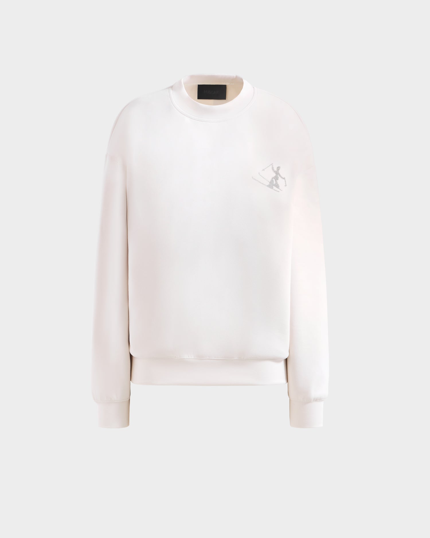 The Rudsak ARIA - 8525661 Vanilla is a women’s white crewneck sweatshirt with long sleeves, ribbed cuffs and hem, and a small ski graphic on the upper left chest—an ideal après-ski pullover. Shown on a light grey background.