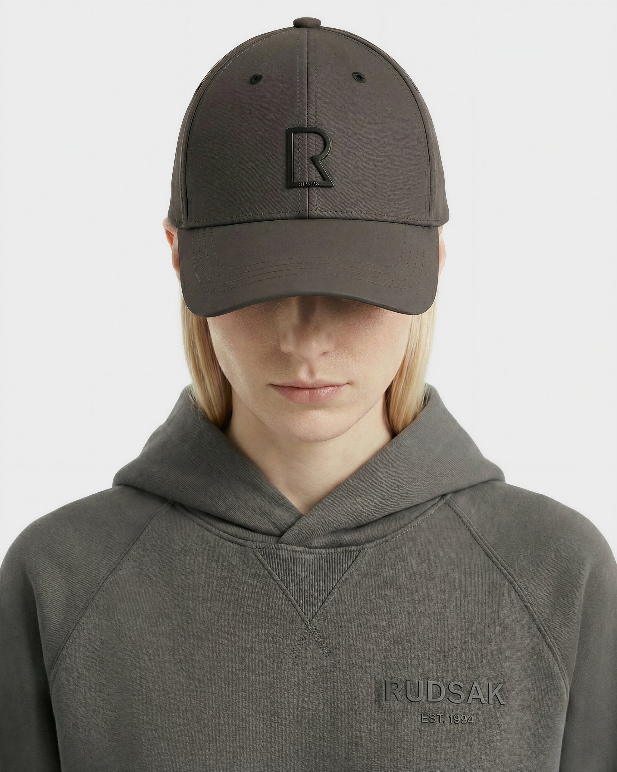 A person wears the Rudsak ARSENE - 9422504 Grey cap with a raised R logo and a matching gray sweatshirt featuring 