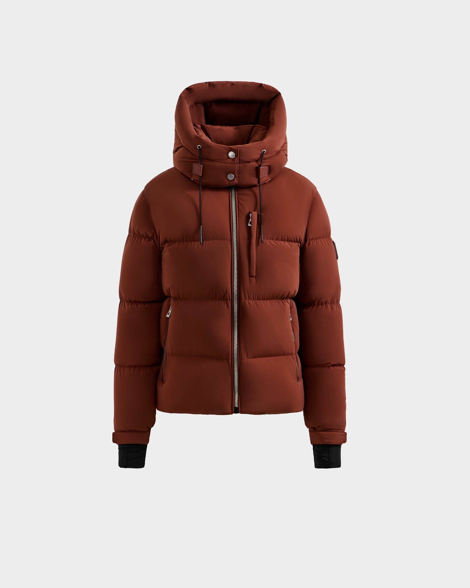 The Rudsak ASHLYN M - 8124564 Rust women's down puffer jacket has a water-resistant shell, high collar, hood, front zipper, snap buttons, side pockets, and black inner cuffs, shown on a plain light grey background.
