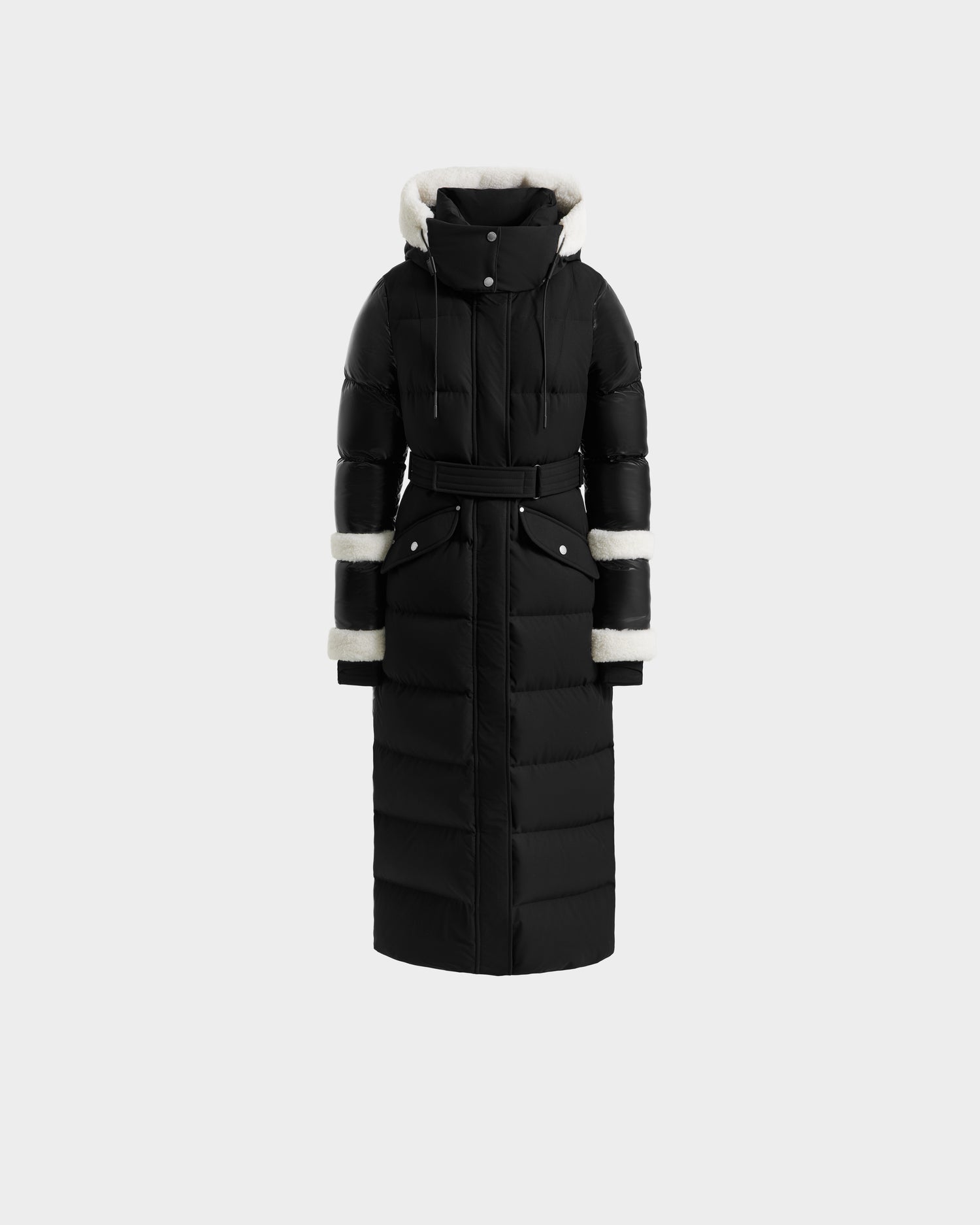 The Rudsak AUDREY XL - 8125601 Black/Iceland is a maxi down puffer with a belted waist, high collar, and hood. Made from recycled Stormshell, it has white faux fur-lined hood, cuffs, and sleeves plus snap buttons and a quilted design.