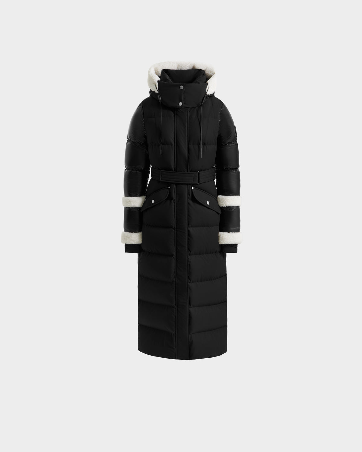The Rudsak AUDREY XL - 8125601 Black/Iceland is a maxi down puffer with a belted waist, high collar, and hood. Made from recycled Stormshell, it has white faux fur-lined hood, cuffs, and sleeves plus snap buttons and a quilted design.