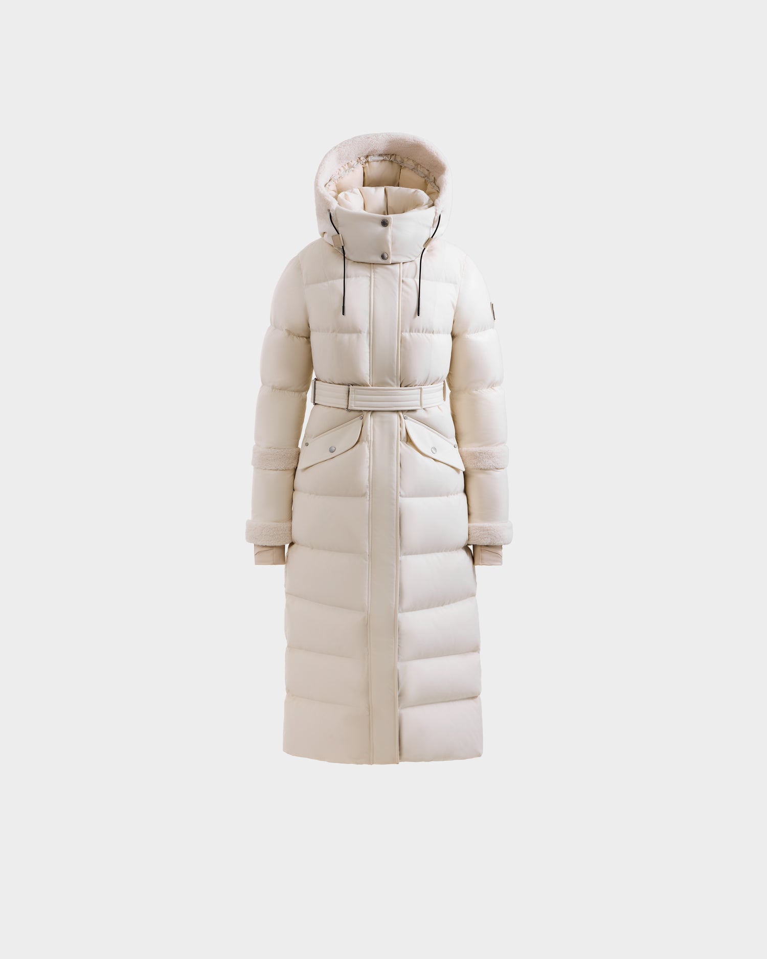 The Rudsak AUDREY XL - 8125601 Vanilla is a maxi-length down puffer with premium insulation, a belted waist, hood, and snap-button pockets, shown against a plain light background.