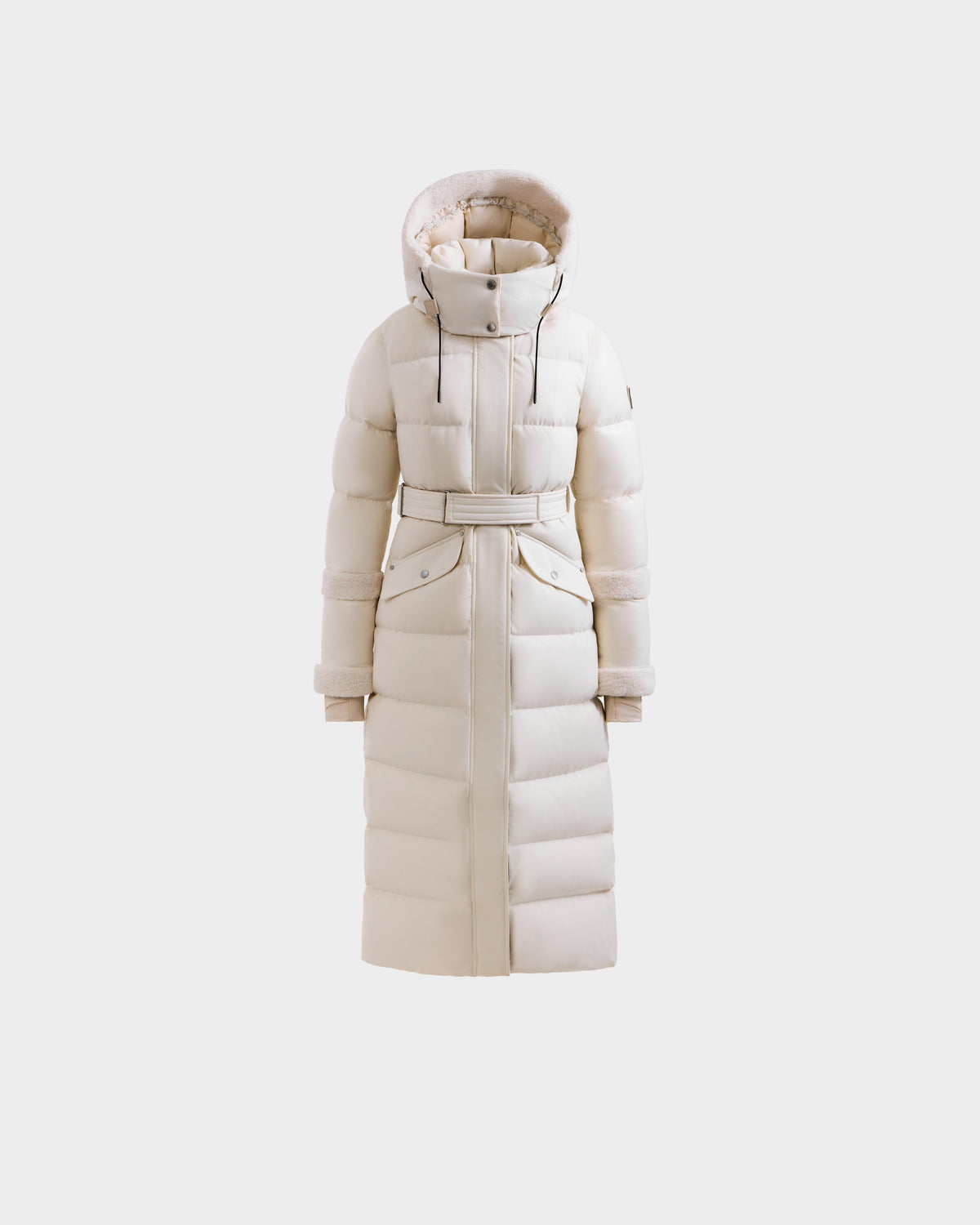 The Rudsak AUDREY XL - 8125601 Vanilla is a maxi-length down puffer with premium insulation, a belted waist, hood, and snap-button pockets, shown against a plain light background.