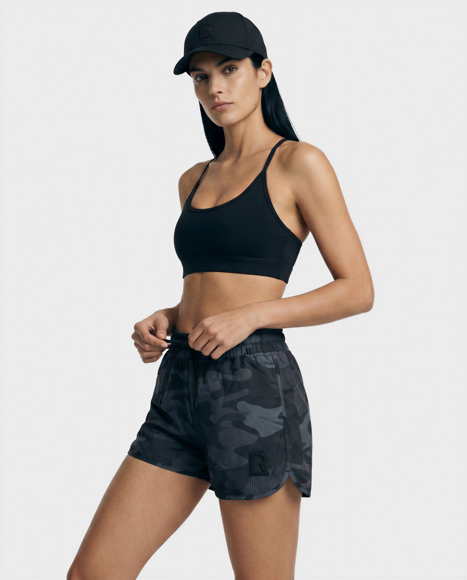 A woman wearing the Rudsak CAPRI - L523009 BLACK sports bra stands against a plain light background, looking at the camera with a neutral expression.