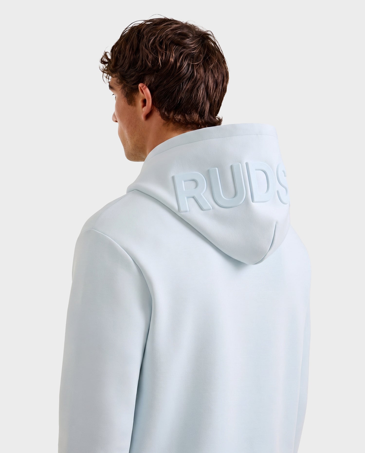 A person seen from behind wears the Rudsak LEROY - U525509 Sky Blue M premium hoodie, featuring "RUDS" embossed on the back of the hood, set against a plain light background.