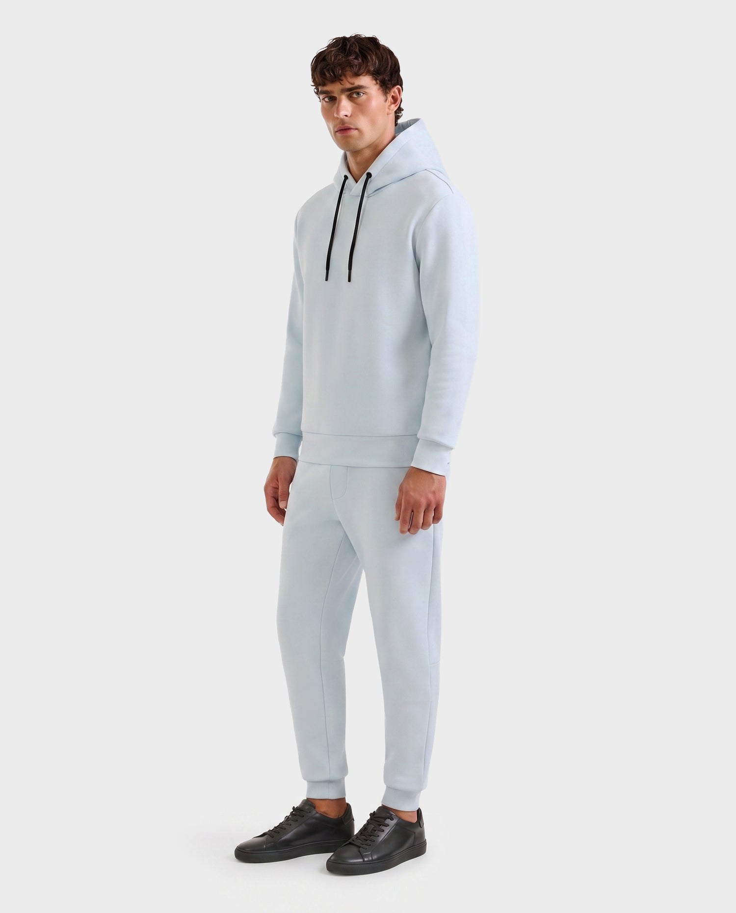 A man wears the Rudsak LEROY - U525509 Sky Blue M hoodie with matching joggers and black sneakers, standing against a plain white background and looking slightly to the side.