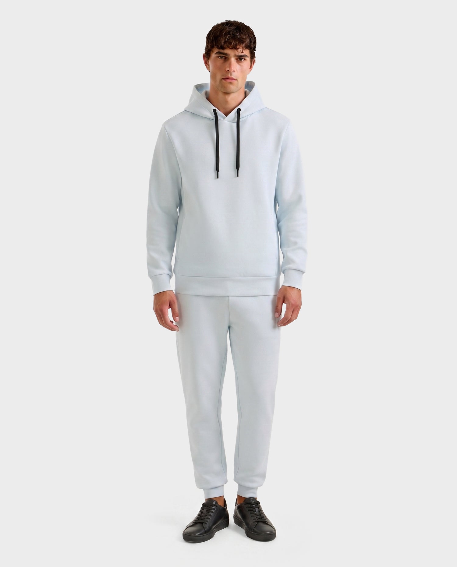 A man faces forward, wearing the Rudsak LEROY - U525509 Sky Blue M unisex hoodie and matching jogger pants with black drawstrings and black sneakers, set against a plain white background.