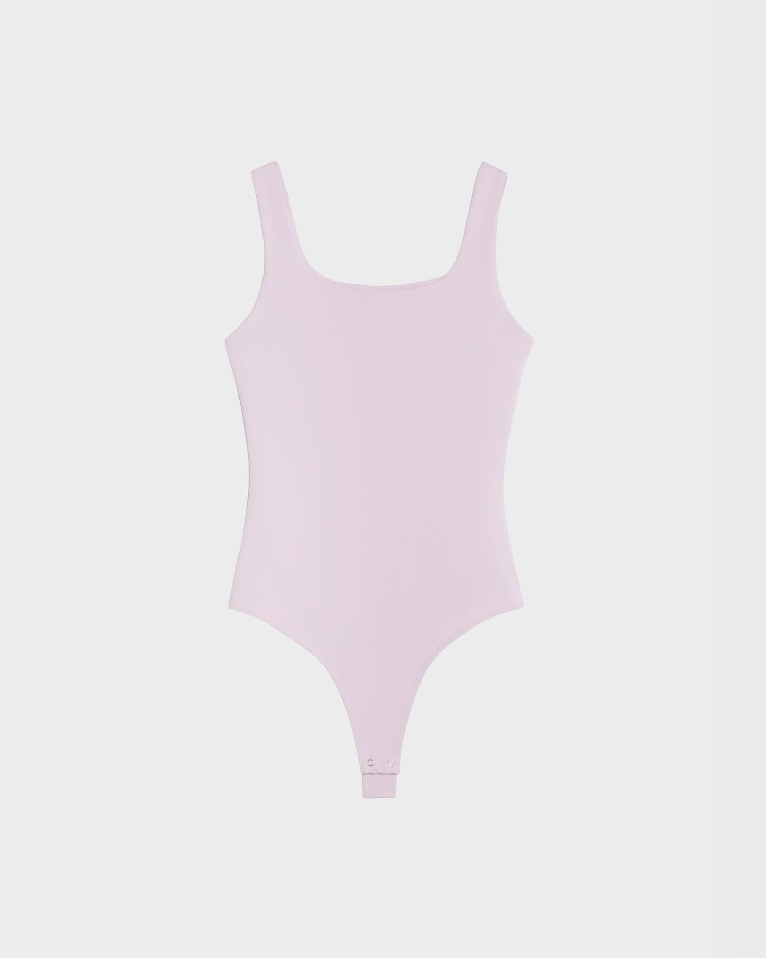 The BRIDGET - 8524033 Lilac Foam by Rudsak is a light pink women’s tank-style bodysuit with a scoop neckline, stretch fabric, and crotch snap closures, shown on a plain white background.