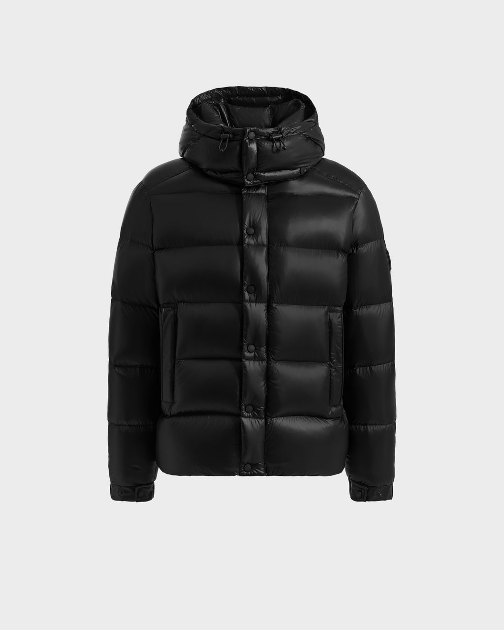 The Rudsak BRAYDEN S - M125525 Black men's winter jacket is a black quilted down puffer with a hood, front zipper with snap buttons, and two large front pockets, shown on a plain light gray background.