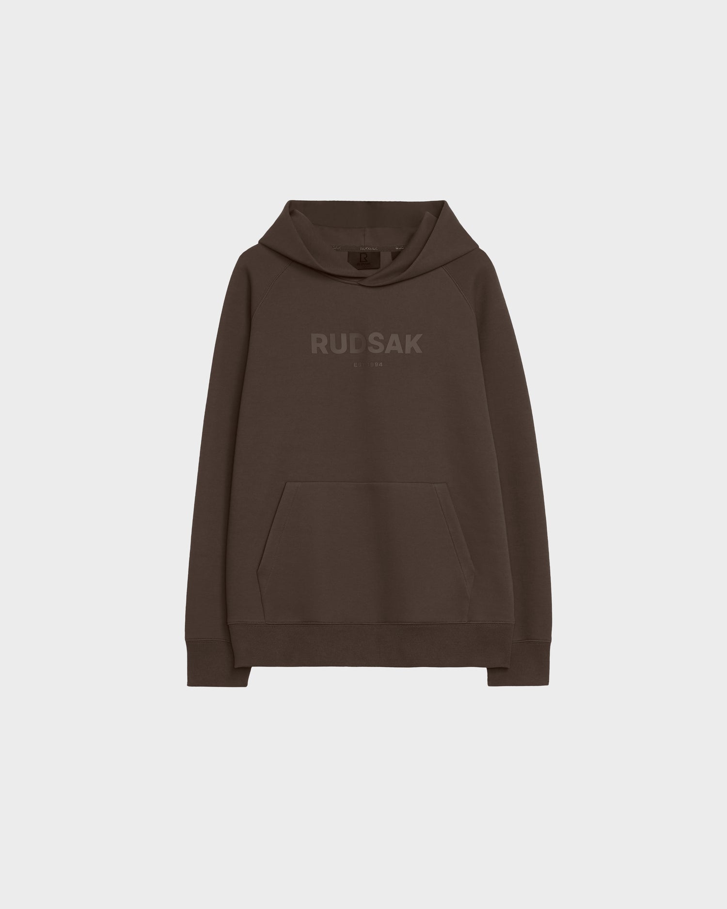 The Rudsak BRIAR - 9525001 Espresso M is a brown unisex hoodie made from a premium cotton blend, featuring a front kangaroo pocket and bold RUDSAK lettering across the chest, styled against a plain light gray background.