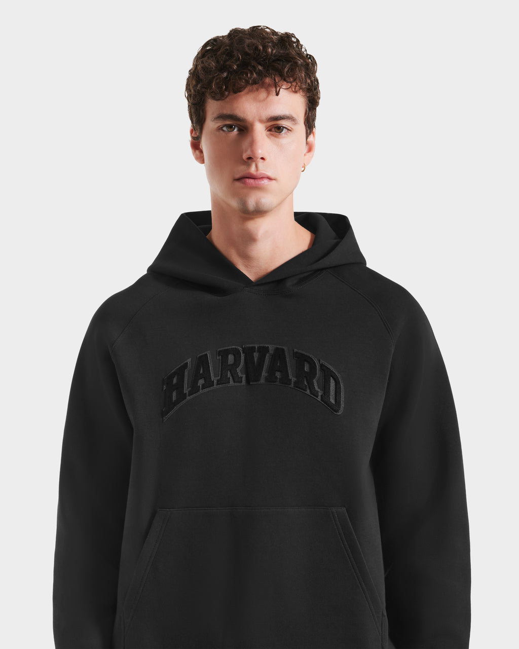 A young man with curly brown hair wears the Rudsak BRIAR B HV - H525509 Black hoodie, featuring bold lettering across the chest, as he stands against a plain white background.