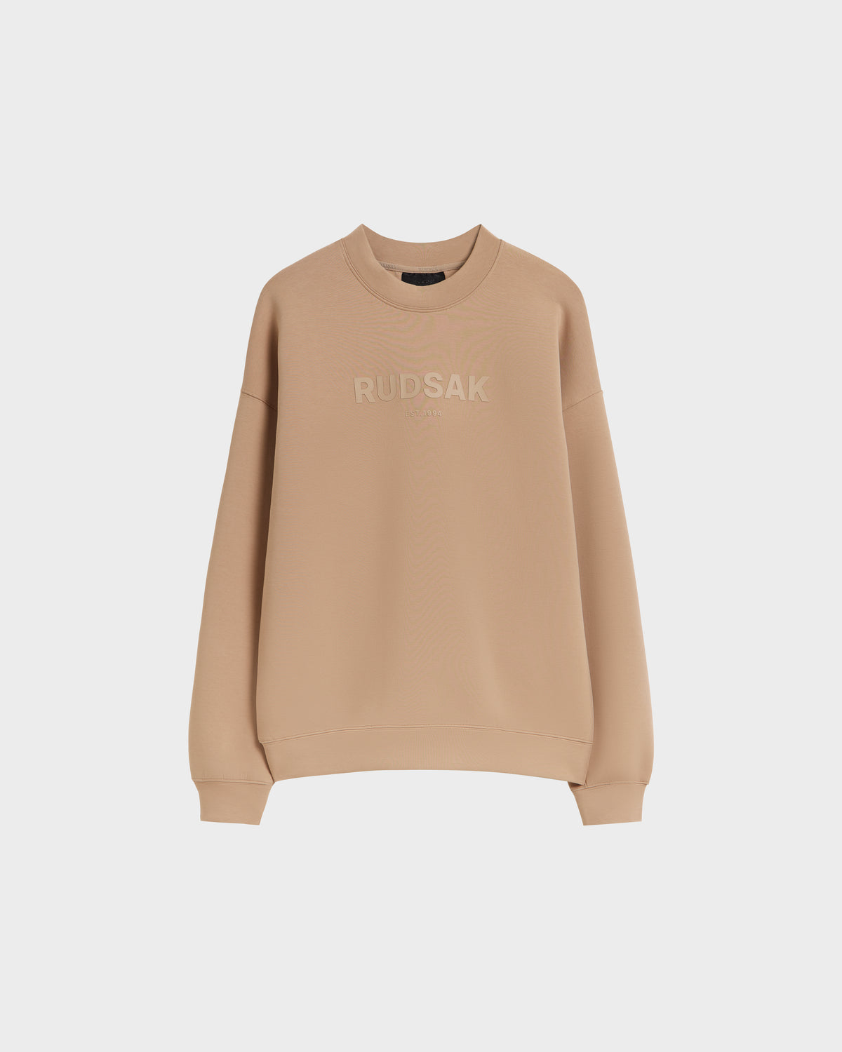 The BRYN - 9524007 Almond M by Rudsak is a beige cotton crewneck sweatshirt with embroidered branding, long sleeves, ribbed cuffs and hem, genderless sizing, shown on a plain white background.