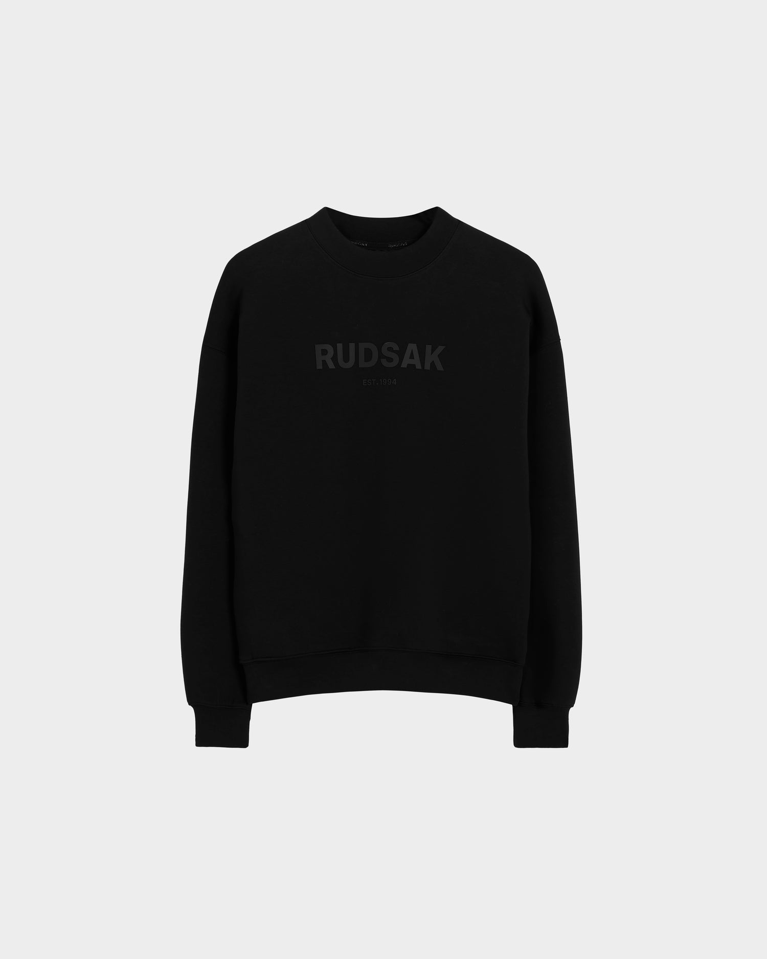 The Rudsak BRYN - 9524007 Black M is a genderless black cotton crewneck sweatshirt with long sleeves and subtle black RUDSAK print on the chest, ideal for everyday wear. Shown against a light gray background.