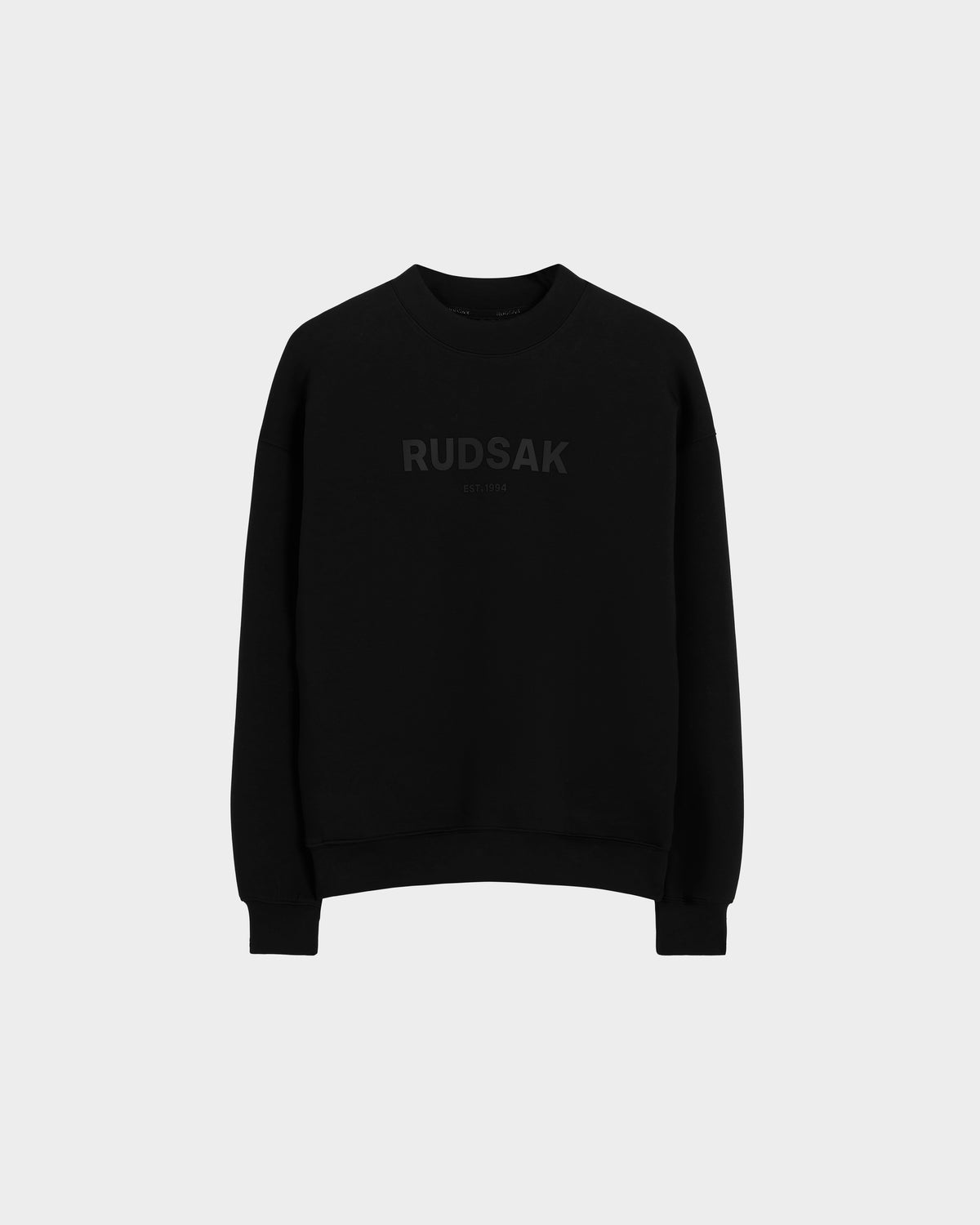 The Rudsak BRYN - 9524007 Black M is a genderless black cotton crewneck sweatshirt with long sleeves and subtle black RUDSAK print on the chest, ideal for everyday wear. Shown against a light gray background.