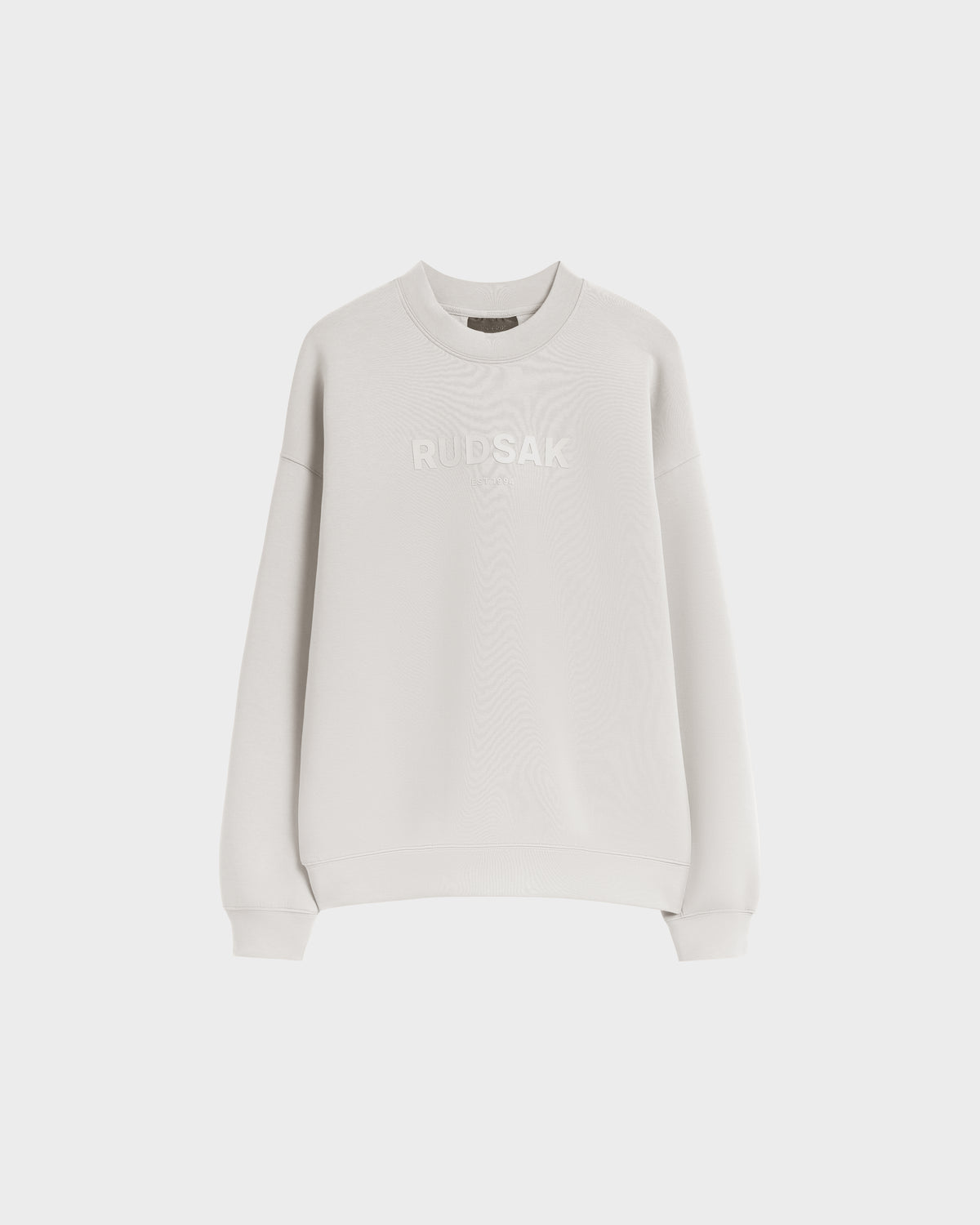 The Rudsak BRYN - 9524007 Vanilla W is a light gray, long-sleeve cotton crewneck sweatshirt with subtle RUDSAK embossing on the chest, crafted for everyday wear and shown against a white background.