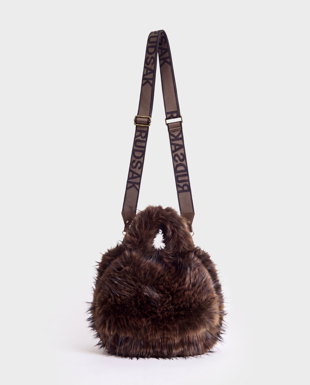 A round, dark brown faux fur Rudsak CABAS - 8325545 Mix Expresso mini tote with a branded adjustable crossbody strap, serving as a perfect statement accessory for winter layers.