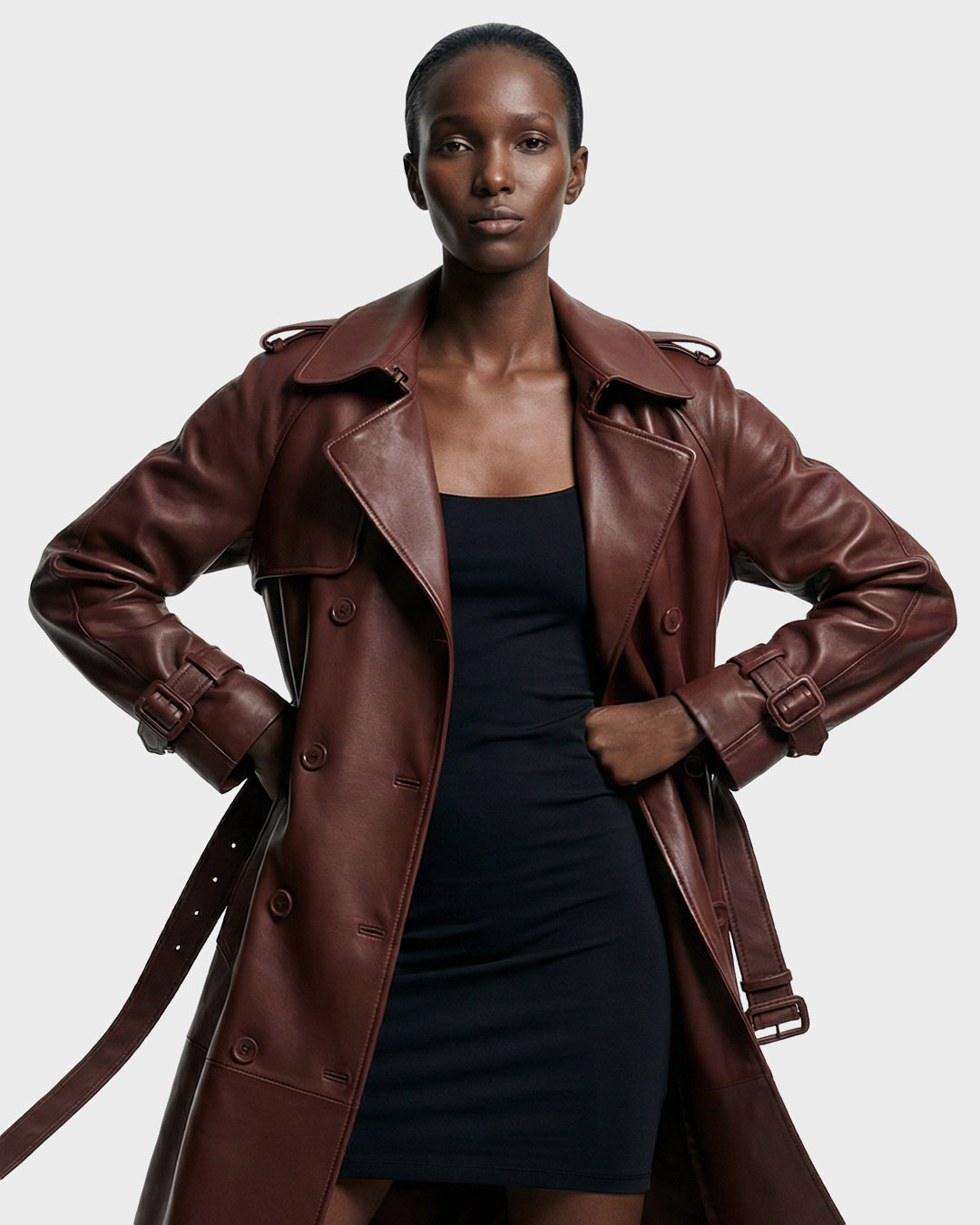 A woman models the Rudsak CASSIE L-B - 8125553 Rust double-breasted trench coat over a fitted black dress, standing confidently with hands on her waist against a plain light background.