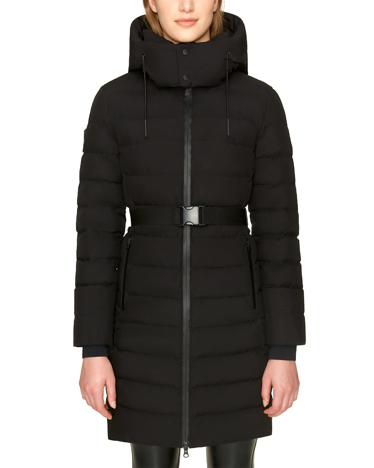A person stands against a white background wearing the Rudsak SAMIRA - 4124503 Black women’s quilted down puffer coat with a removable hood, belted waist, front zipper, zippered pockets, and horizontal quilting for extra warmth.
