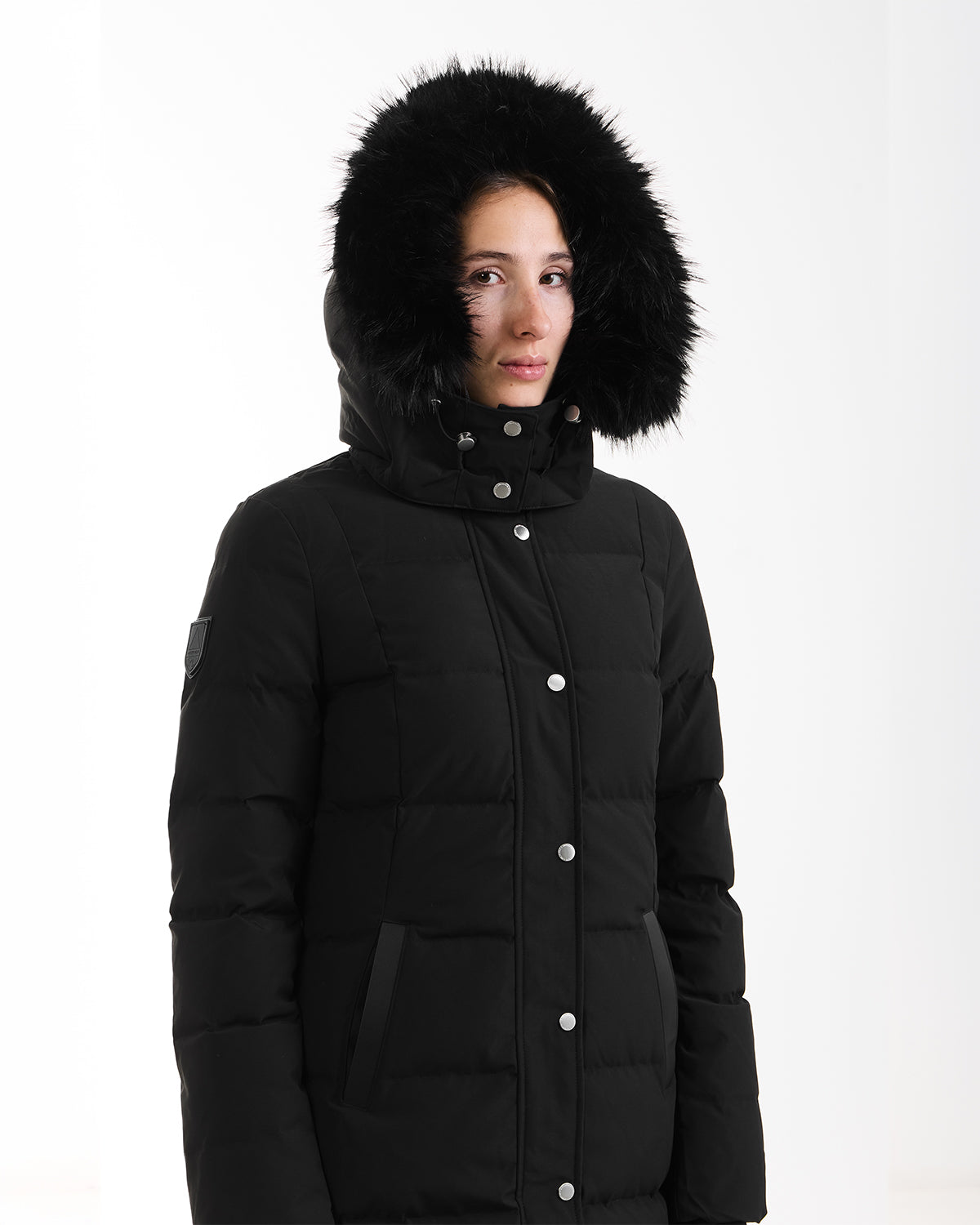 A person wearing the Rudsak JANET - 4125504 Black quilted down puffer jacket with a removable faux fur collar and premium insulation stands against a plain white background.