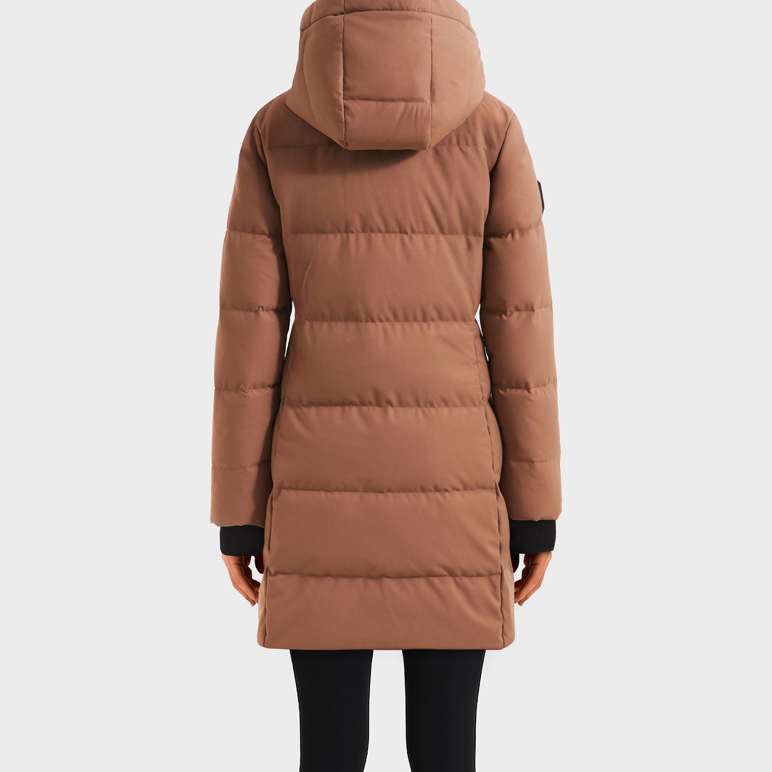 A person wearing the Rudsak SYDNEY COM - 4123511 Taupe long hooded parka with water-repellent duck down, horizontal stitching, and black cuffs, paired with black pants, is shown standing with their back to the camera.