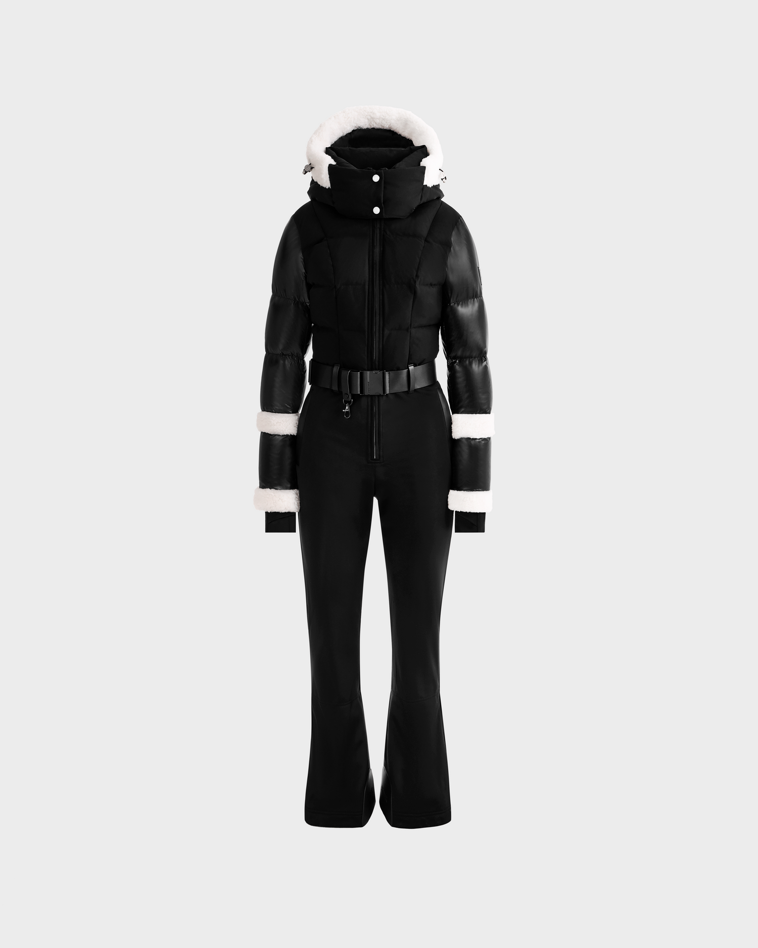 The Rudsak CARMEN - 8125708 Black one-piece ski suit features a fitted silhouette, flared pants, padded jacket, and white fur trim on the hood, sleeves, and cuffs, displayed on a plain light gray background.