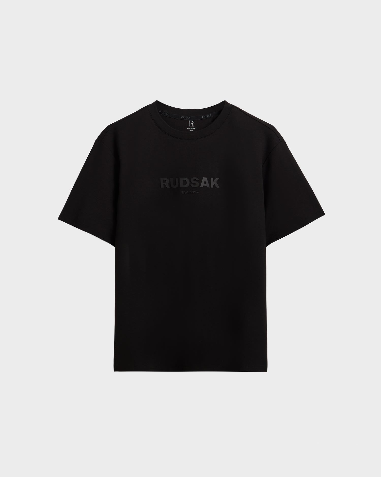 The CASEY - 6525037 Black by Rudsak is a men's plain black T-shirt featuring "RUDSAK" subtly printed in dark letters across the chest, shown on a light gray background.