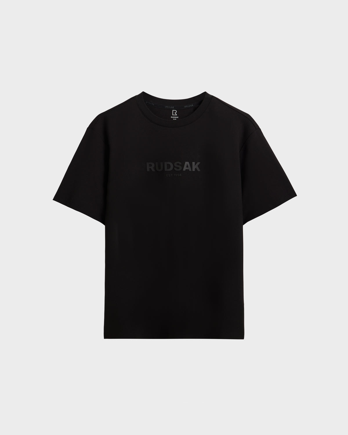 The CASEY - 6525037 Black by Rudsak is a men's plain black T-shirt featuring "RUDSAK" subtly printed in dark letters across the chest, shown on a light gray background.