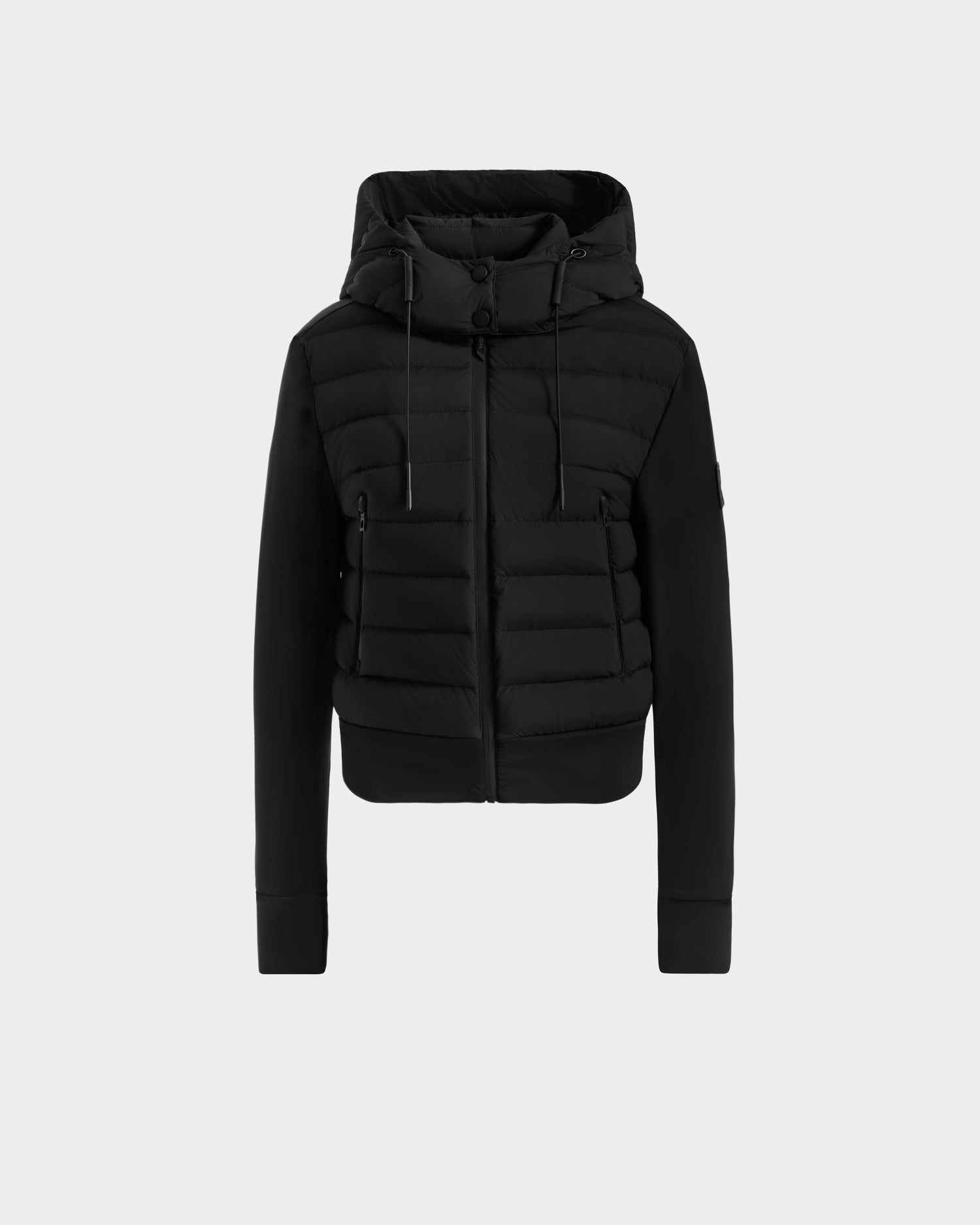 The Rudsak CASSA - 8125057 Black is a women’s waterproof hooded puffer jacket with front zipper, ribbed cuffs, drawstring hood, and horizontal quilting. Shown on a plain light grey background, it’s ideal for transitional weather.