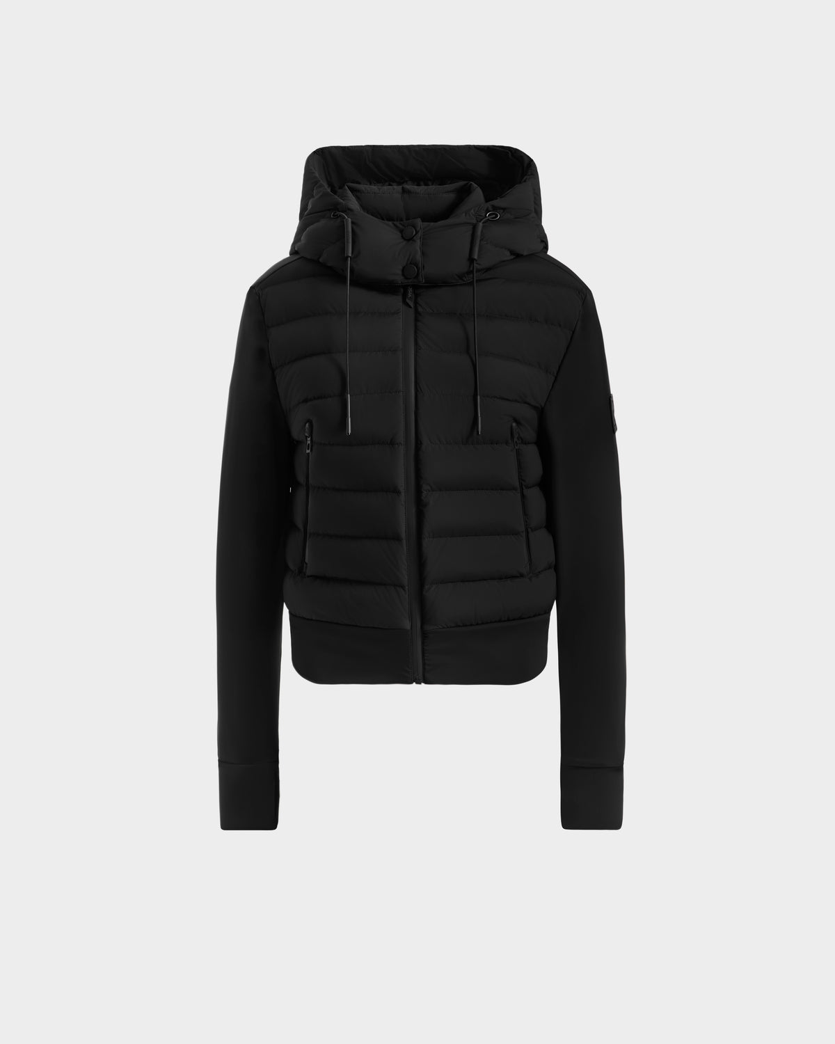 The Rudsak CASSA - 8125057 Black is a women’s waterproof hooded puffer jacket with front zipper, ribbed cuffs, drawstring hood, and horizontal quilting. Shown on a plain light grey background, it’s ideal for transitional weather.