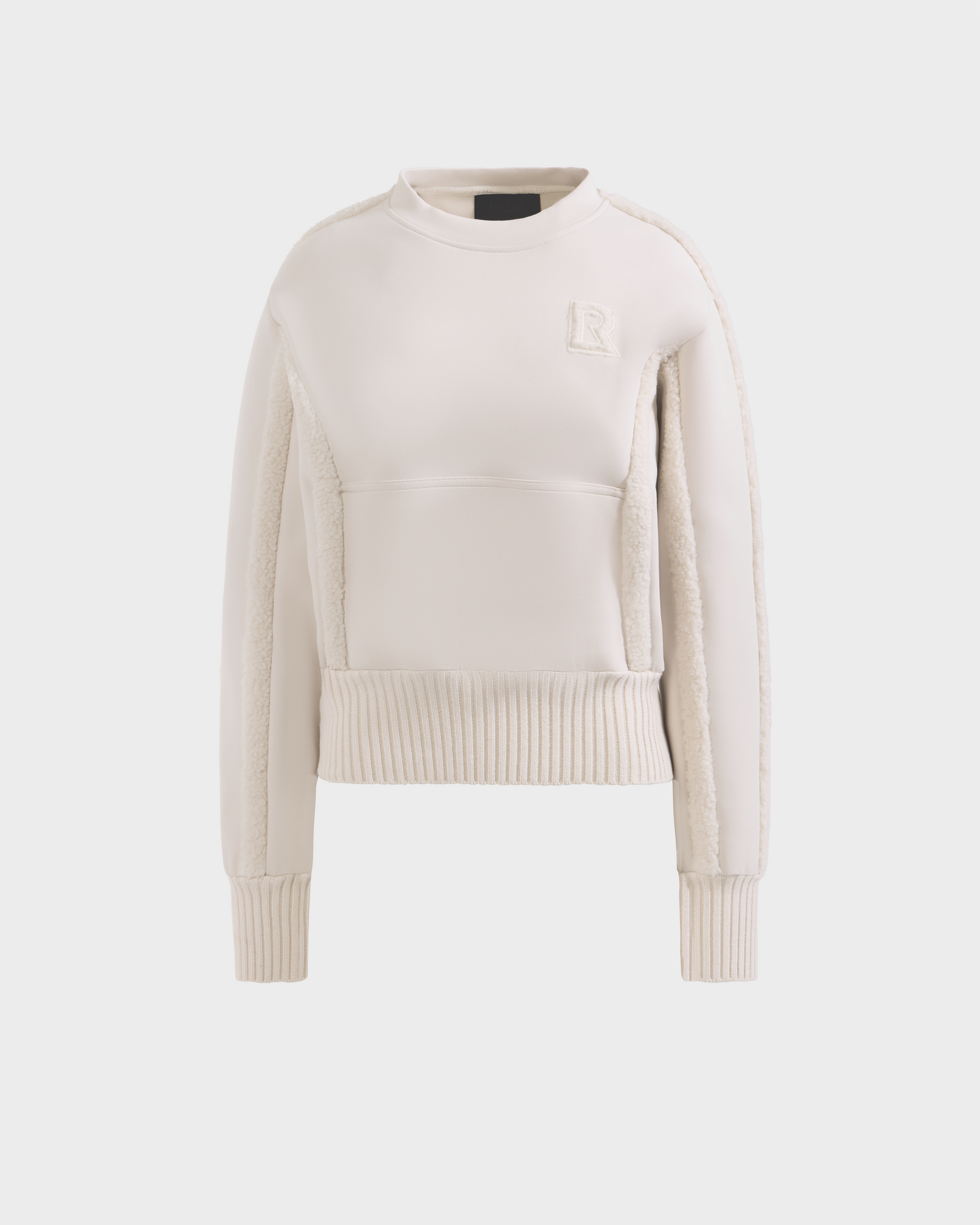 The CHANA - 8525656 Vanilla by Rudsak is a cream women’s crew neck sweatshirt with ribbed cuffs and hem, textured side panels, and embossed R logo on the chest, offering après-ski chic style. Shown on a plain white background.