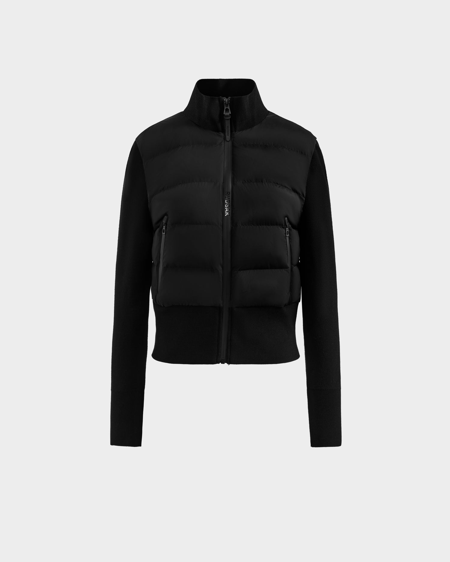 The Rudsak CLAREMONT - 8125502 Black is a women’s hybrid down jacket with a high collar, quilted front, smooth long sleeves, two waterproof zippered pockets, and a fitted waist, shown against a plain light gray background.