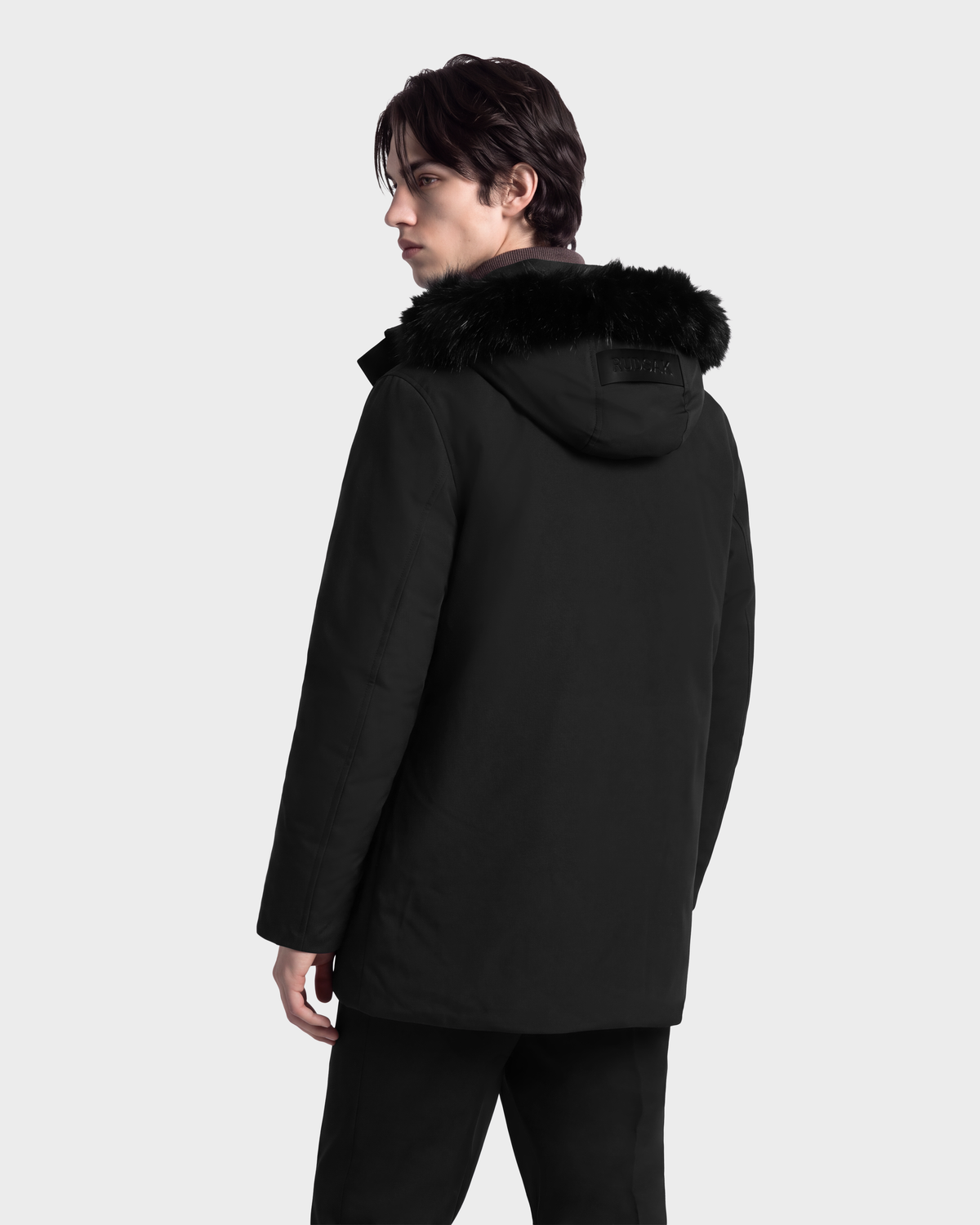 A man viewed from behind, wearing a black Rudsak EDWARD - 6126501 Black deep-winter parka with a faux fur trim.