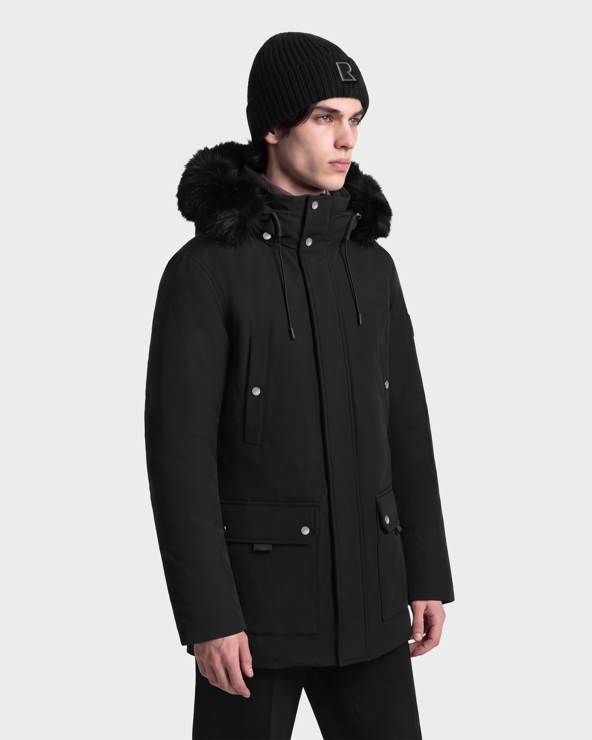 A man wearing an EDWARD - 6126501 Black deep-winter parka with a fur-trimmed hood and a matching knit beanie.