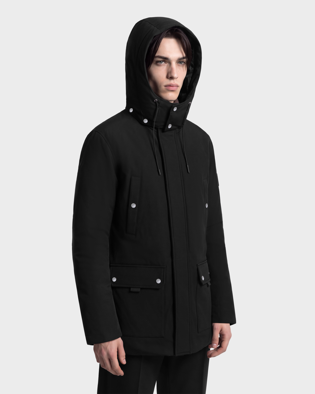 A person wears a black RUDSAK EDWARD - 6126501 Black extreme winter hooded parka with silver snap buttons and four front pockets.