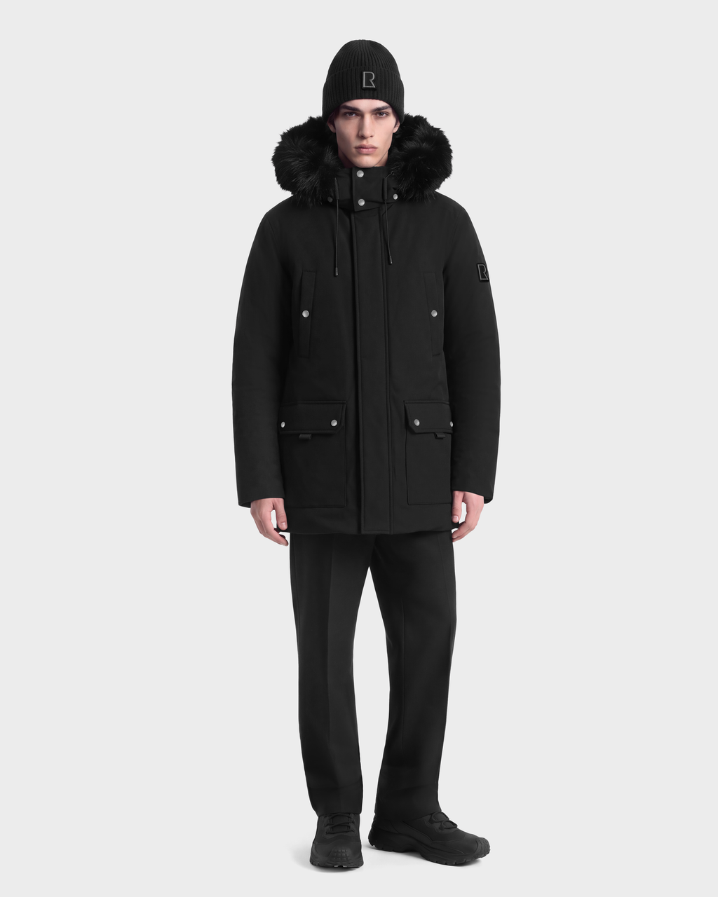 A man wearing a black EDWARD - 6126501 Black parka with a fur-trimmed hood and a matching beanie.
