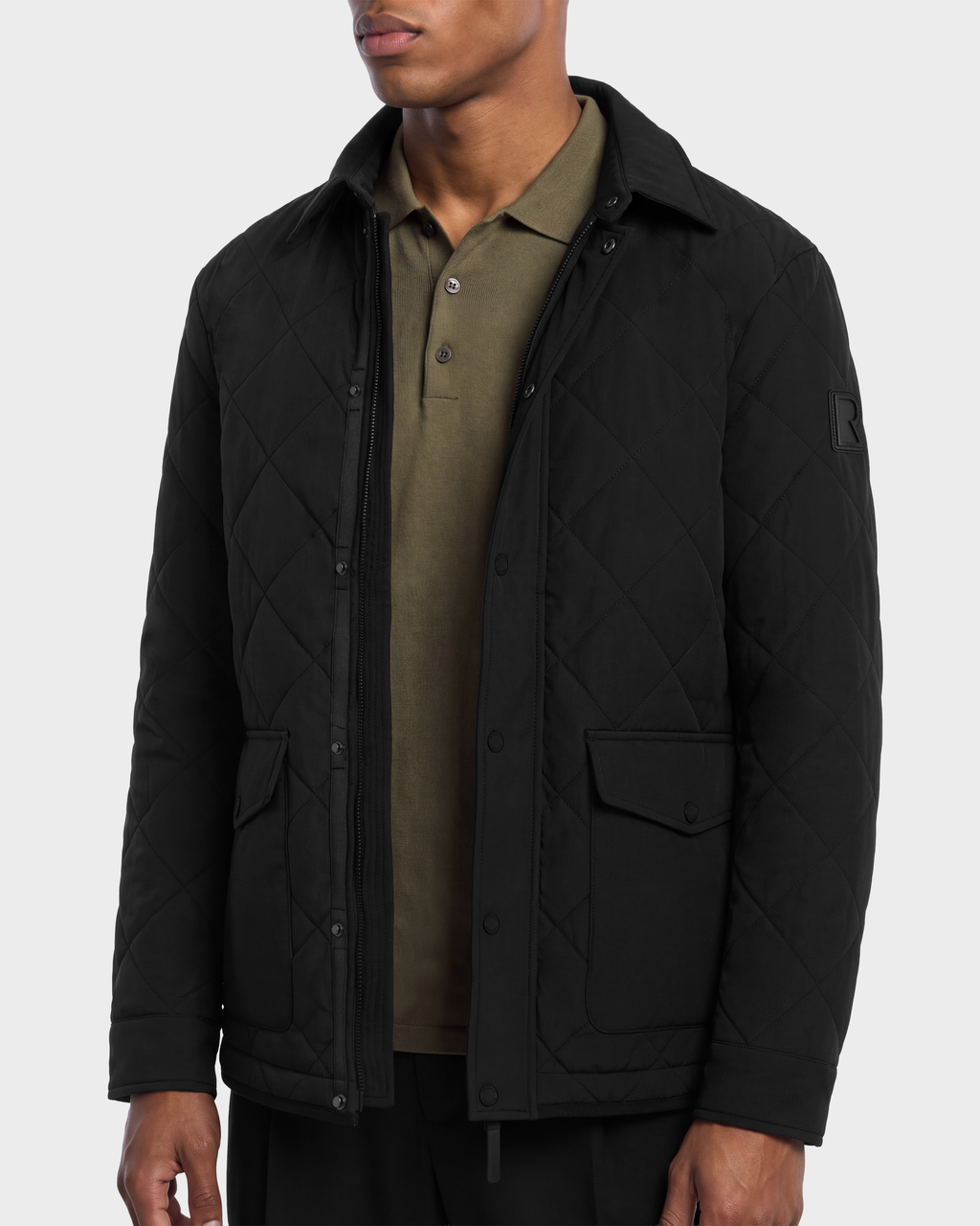 A person wearing a black Rudsak HENDRIX - 6126721 quilted jacket with a collared neckline, a button-down front, and two flap pockets over an olive green polo shirt.