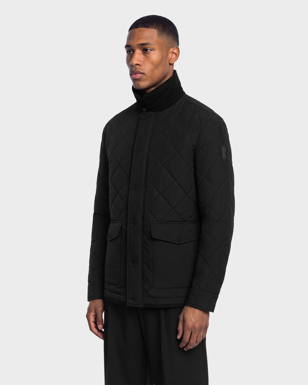 A man wearing a black Rudsak HENDRIX - 6126721 Black quilted jacket with a high collar and front snap buttons.