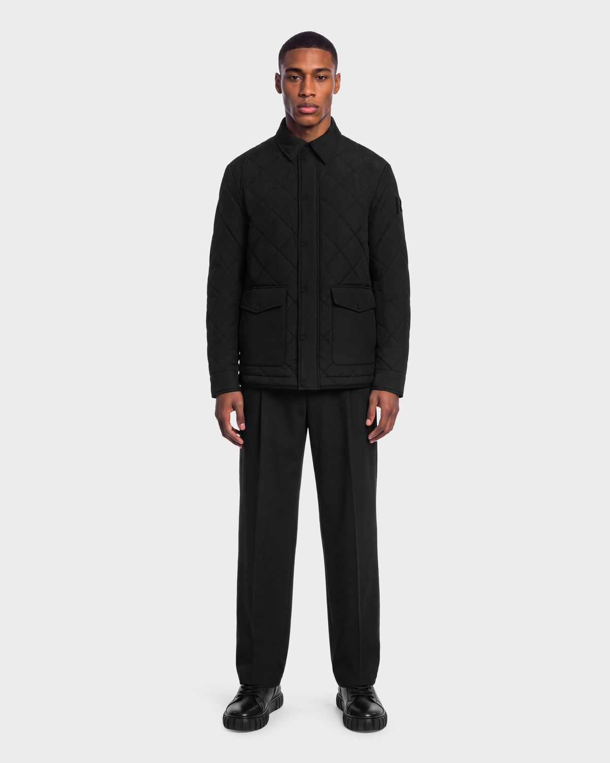 A man wearing a black Rudsak HENDRIX - 6126721 Black quilted button-down jacket, black trousers, and black shoes.