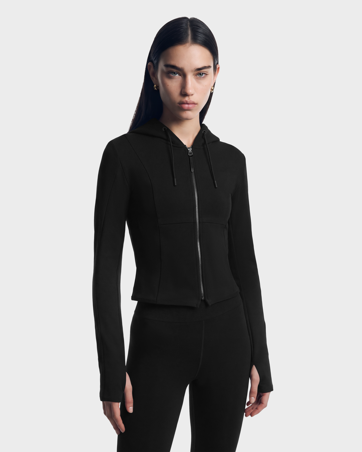 A person wearing the JUNIPER - 8526679 Black/Black, a black, fitted zip hoodie with a cropped silhouette and thumbhole cuffs.